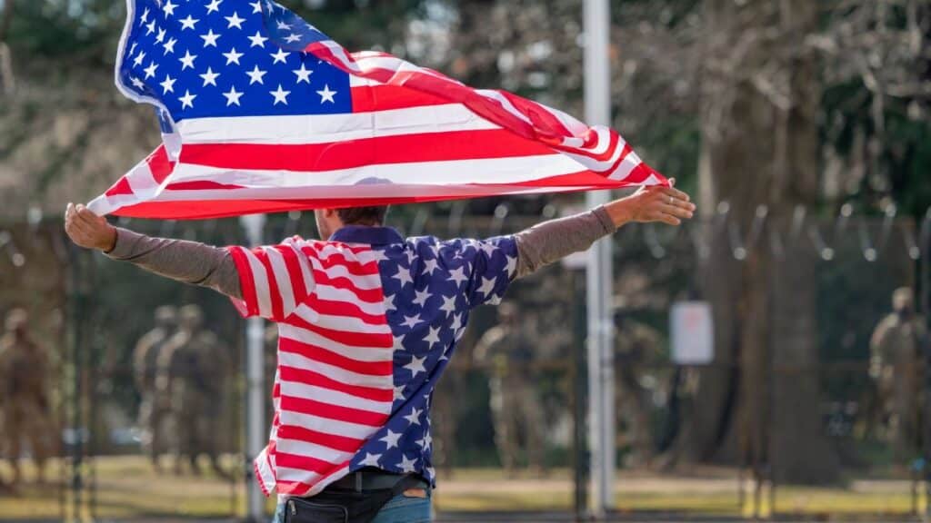 Man wearing American flag shirt and holding flag in Washington DC, symbolizing patriotism.