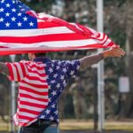 Man wearing American flag shirt and holding flag in Washington DC, symbolizing patriotism.