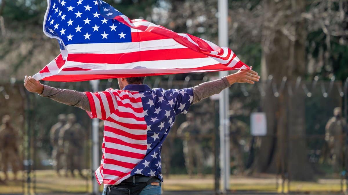 Man wearing American flag shirt and holding flag in Washington DC, symbolizing patriotism.