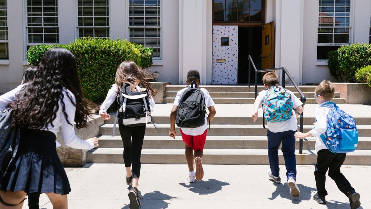 Group of students with backpacks running into school, captured from behind, showing excitement.