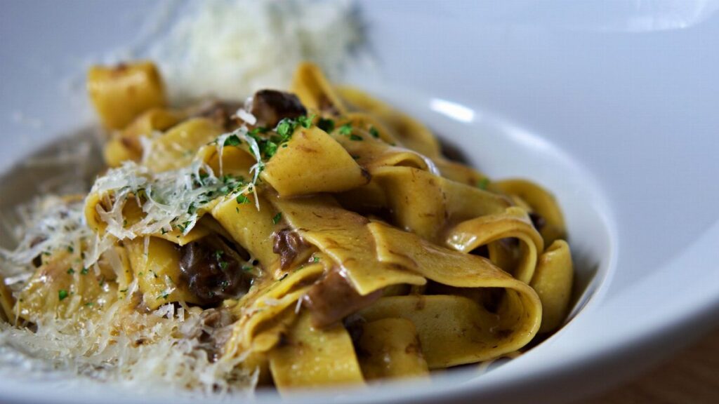 Close-up of pappardelle pasta topped with parmesan cheese and mushrooms, perfect for Italian cuisine lovers.
