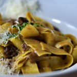 Close-up of pappardelle pasta topped with parmesan cheese and mushrooms, perfect for Italian cuisine lovers.