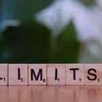 Wooden letter tiles forming the word 'LIMITS' on a wooden table.