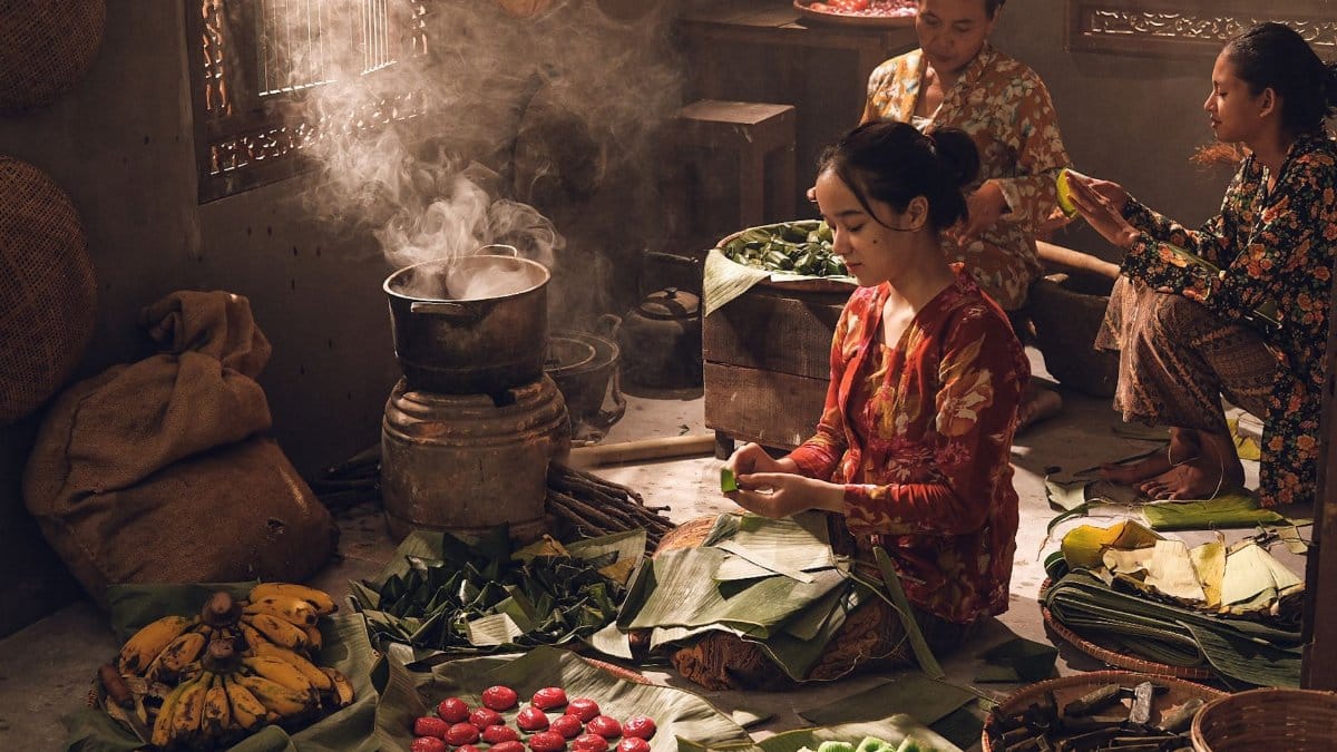 Women prepare traditional Asian food using banana leaves in a rustic kitchen setting.