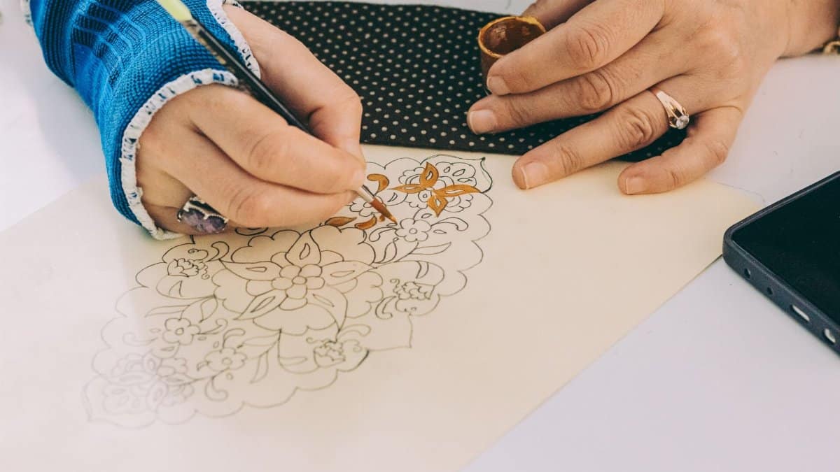 Decorative hand painting on fabric, highlighting intricate floral design with an artist wearing a wrist cast.