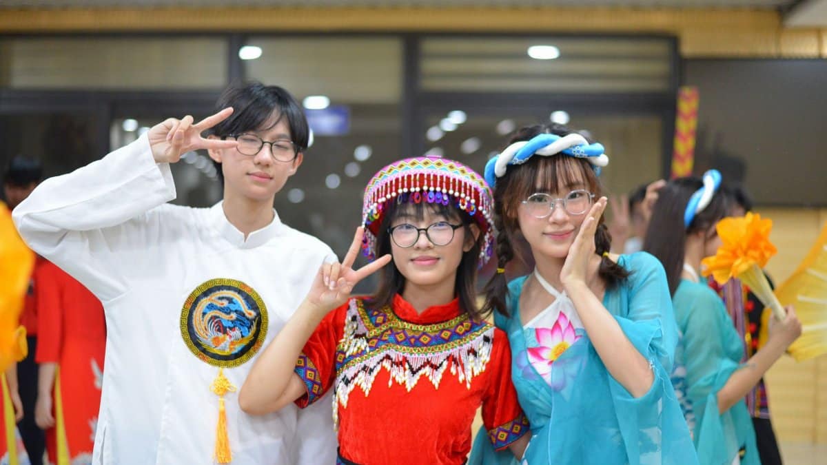 Three people in colorful traditional outfits at an indoor cultural festival.