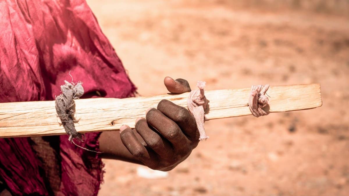 Detailed shot of a hand grasping a wooden plank with tied fabrics in Timokten, Algeria.