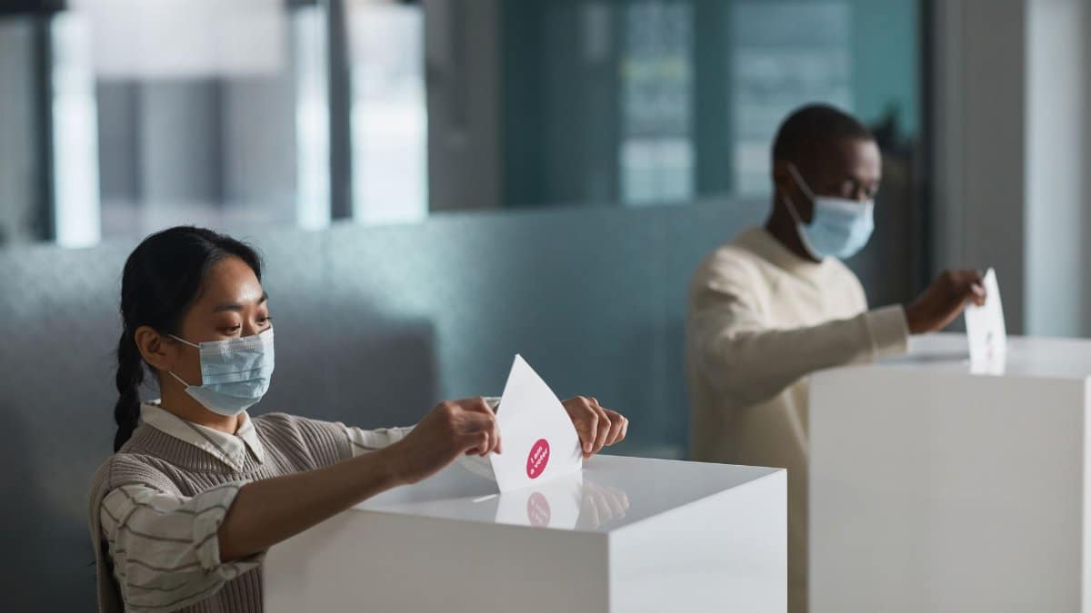 People casting ballots in an indoor election setting, practicing safety measures with masks.