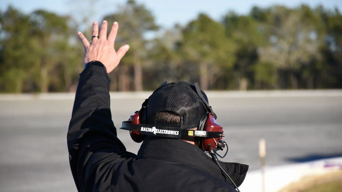 Motorsport official raising hand on track, signaling during race event.