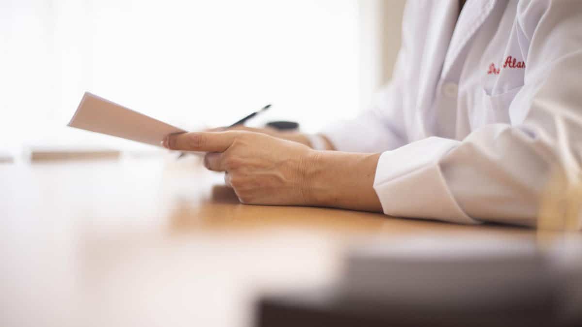 Close-up of a doctor in a lab coat reviewing paperwork at a desk.