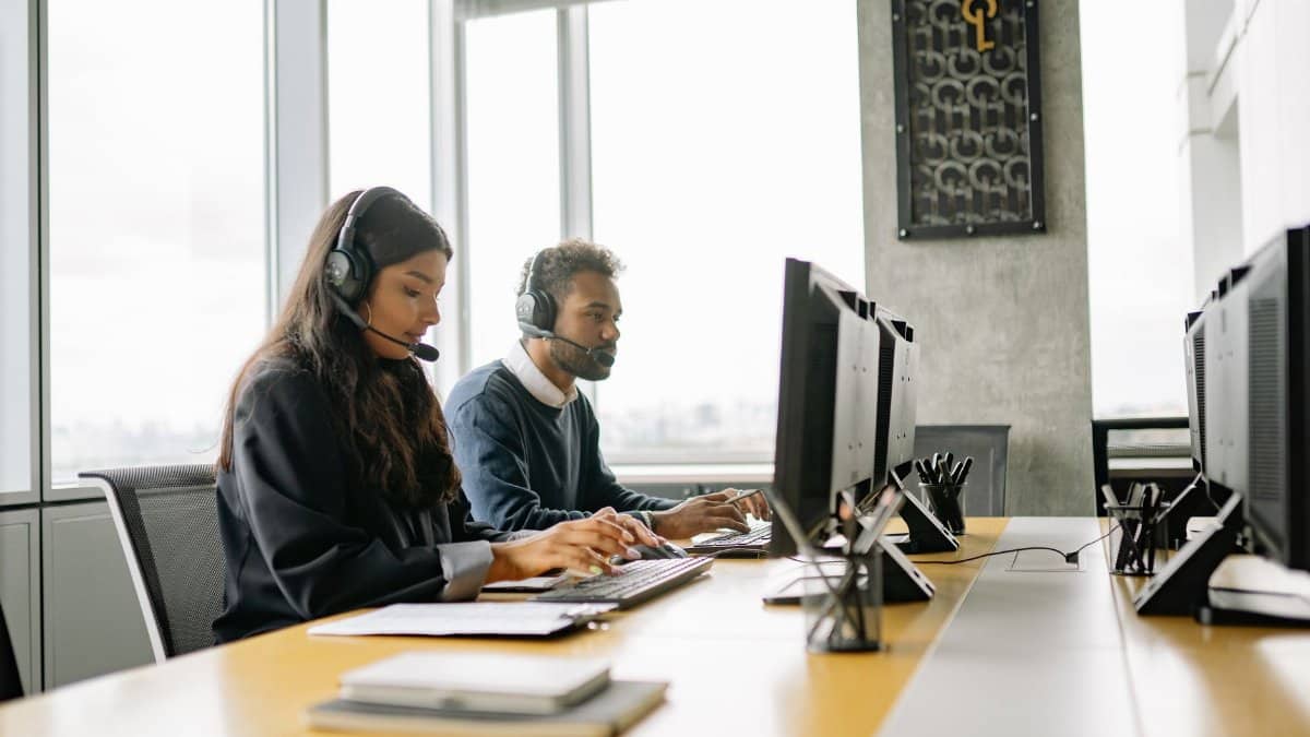 Two customer service representatives wearing headsets working at computers in a modern office.