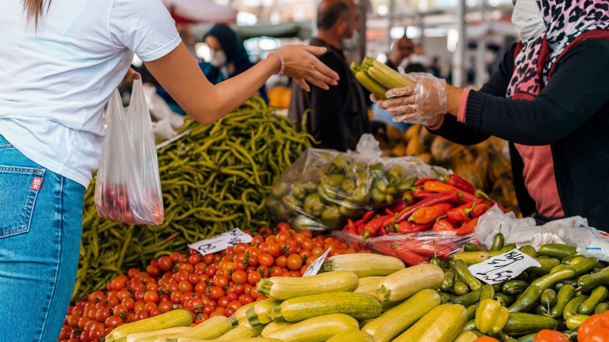 Colorful scene of a customer buying fresh vegetables from a vendor at a bustling farmers market.