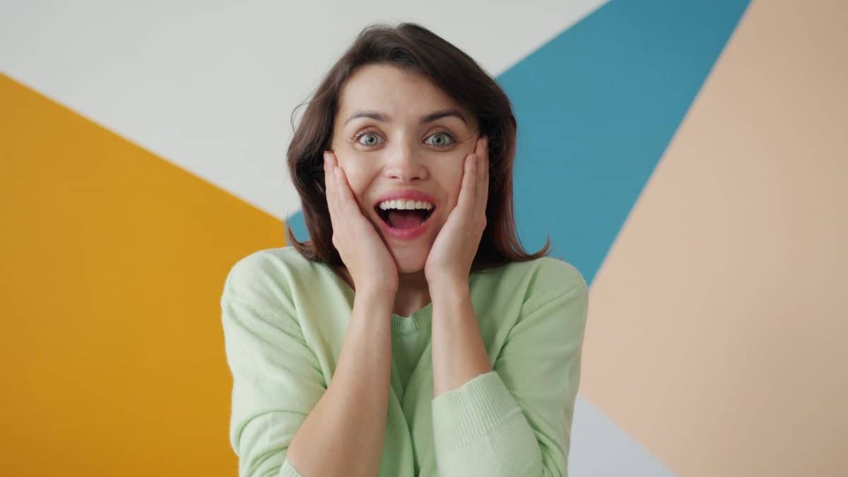 Cheerful woman expressing surprise against a colorful geometric background.