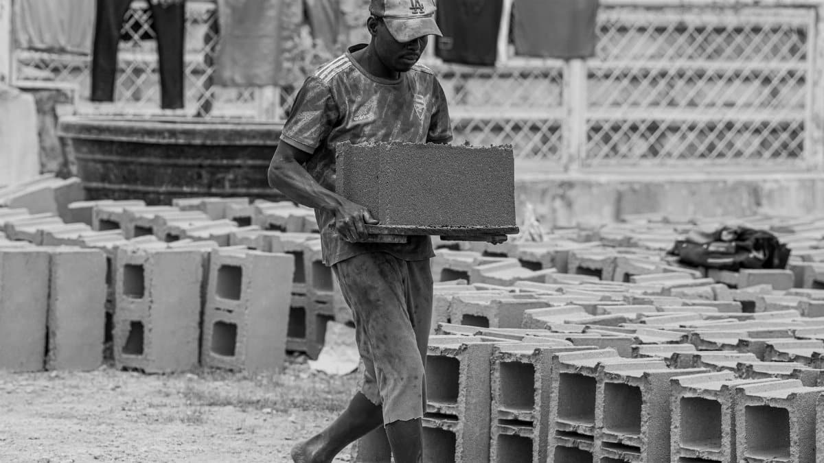 A laborer carries a concrete block on a construction site in Kaduna, Nigeria. Black and white. Manual labor.