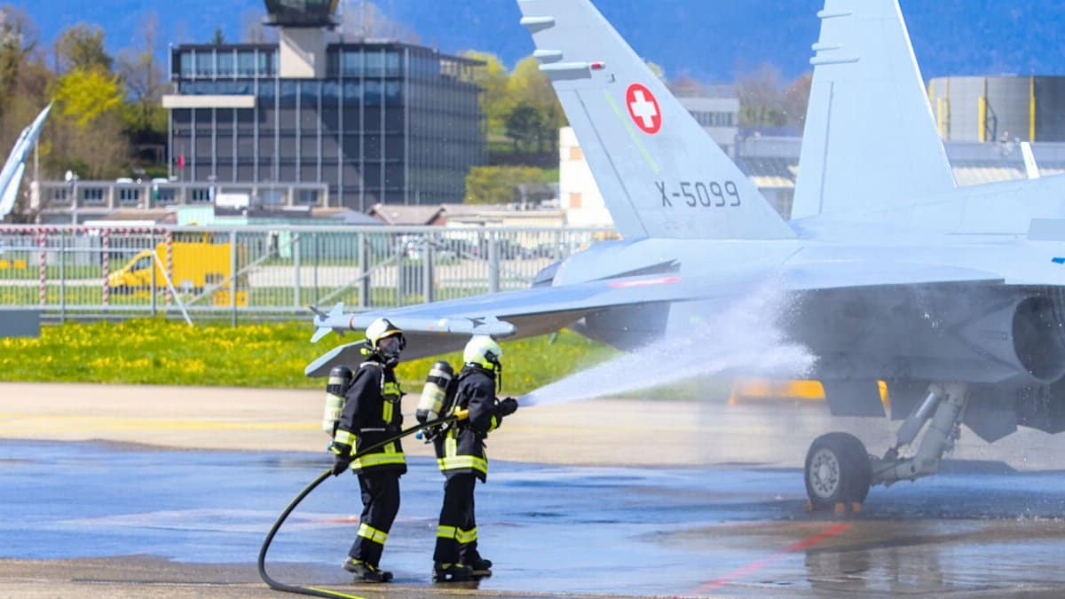 Firefighters conduct a training exercise with a military aircraft on a Swiss airfield.