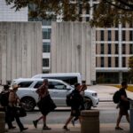 People crossing the street in Dallas in front of a modern office building on a sunny day.
