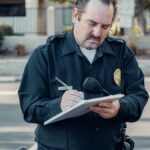 Police officer in uniform writing a ticket on a clipboard outdoors.