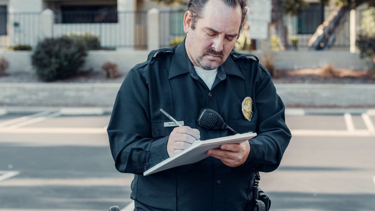 Police officer in uniform writing a ticket on a clipboard outdoors.