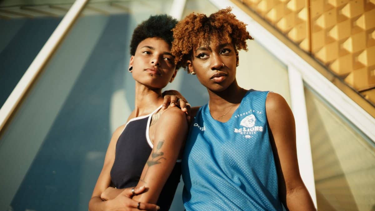 Two black women with short curly hair in sportswear pose stylishly outdoors