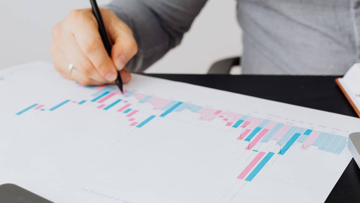 Close-up of a man writing on a printed chart indoors, analyzing colorful data.