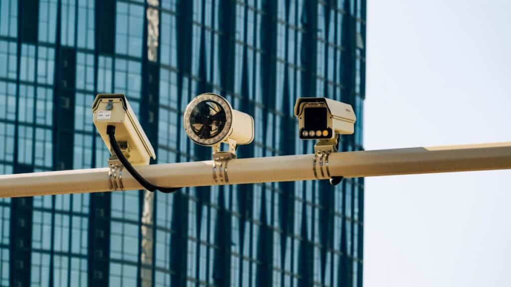 Surveillance cameras mounted on a pole in front of a modern glass building.