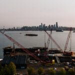 Aerial view of Seattle harbor with cranes and city skyline at day.