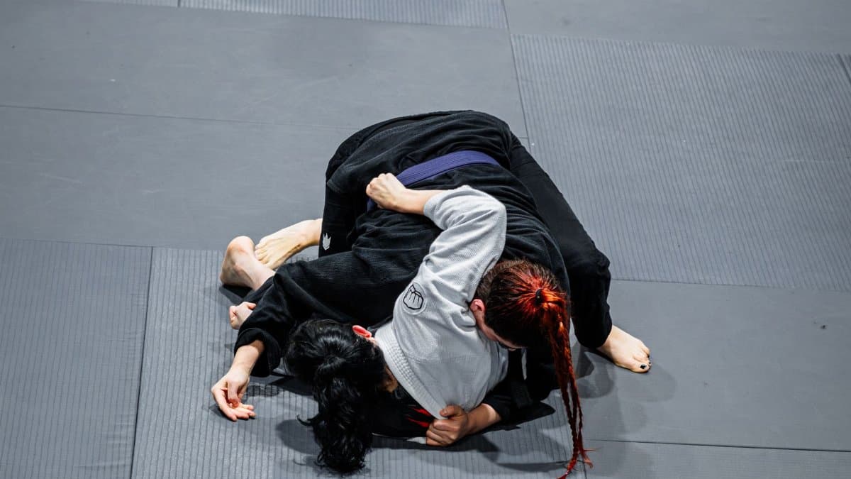 Two women engage in a competitive Brazilian Jiu-Jitsu match on a gym mat, showcasing technique and strategy.