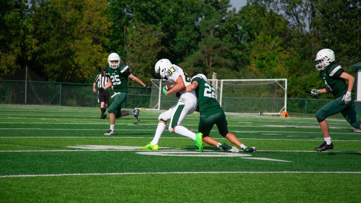 Intense tackle during a high school football match on a sunny day.