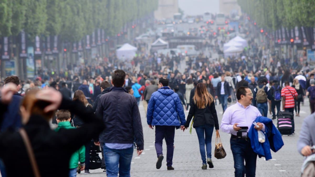 A vibrant crowd walking on the famous Champs-Élysées in Paris, with the Arc de Triomphe in the background.