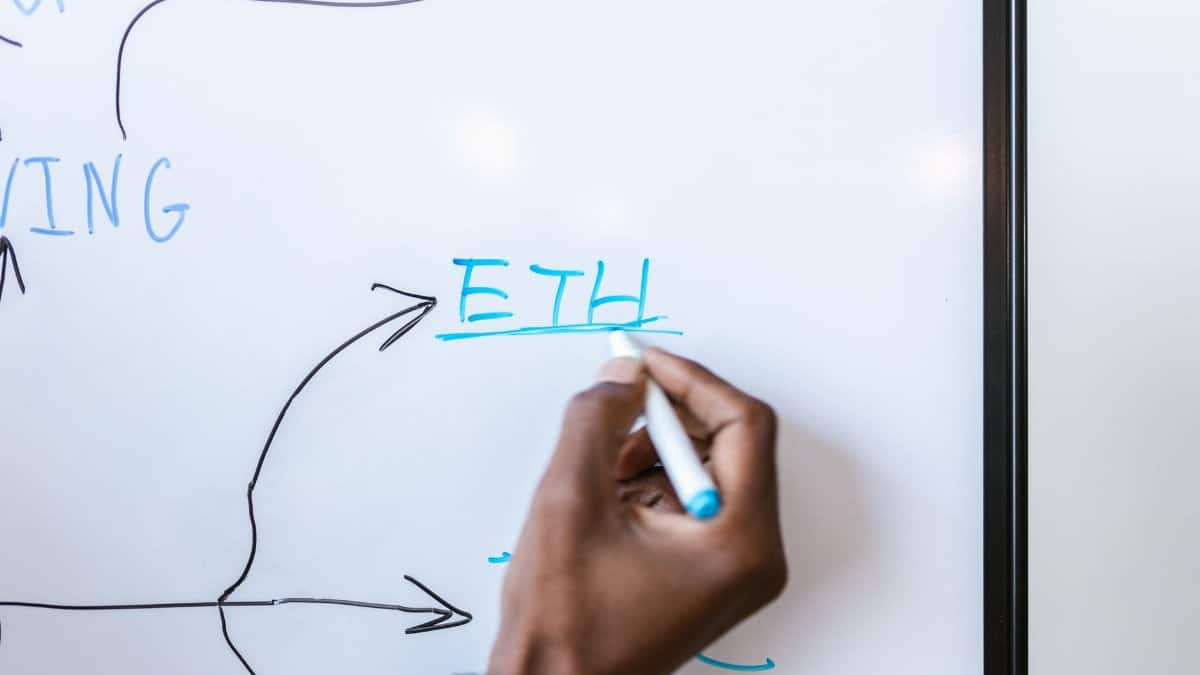 Hand writing 'ETH' on a whiteboard, highlighting Ethereum concept.