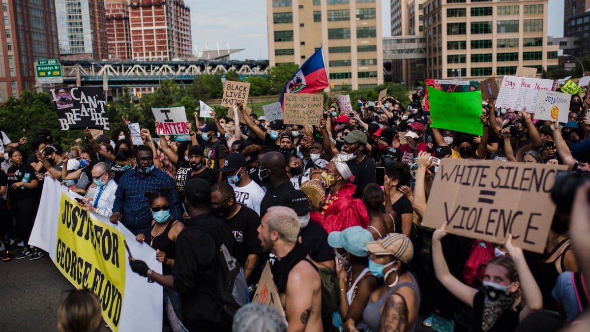 Crowd of activists protest for George Floyd justice, holding signs in a city street.