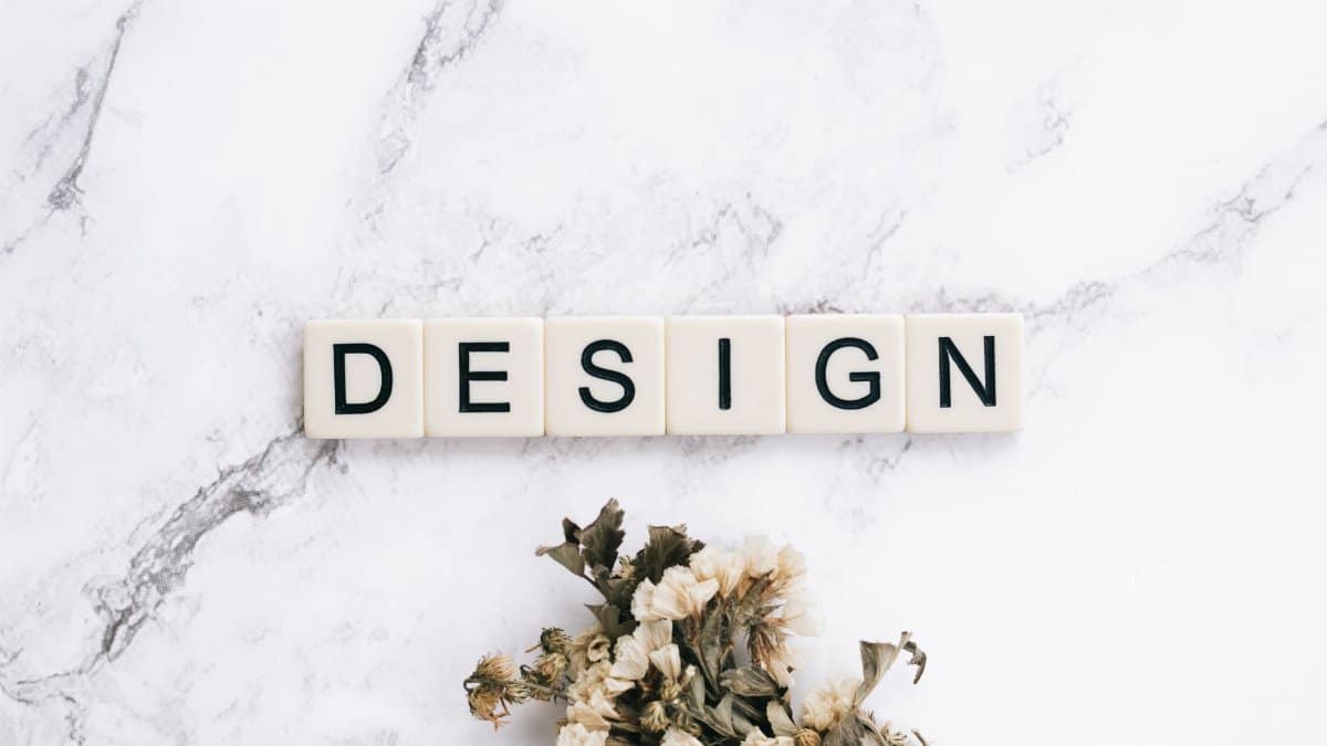 Close-up of Scrabble tiles spelling 'design' on marble with flowers.