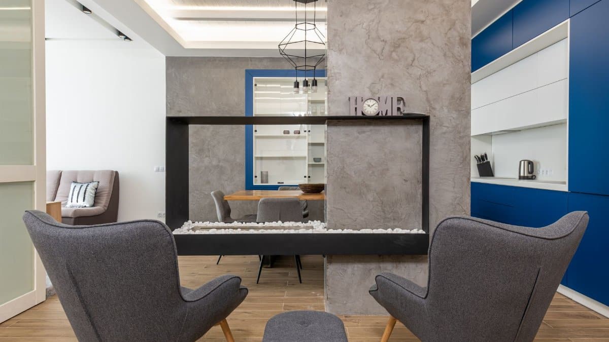 Modern design of studio apartment with comfortable armchairs placed near fireplace in kitchen with minimalist interior