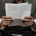 Close-up of a prisoner in uniform reading a letter in a cell setting, highlighting prison life.