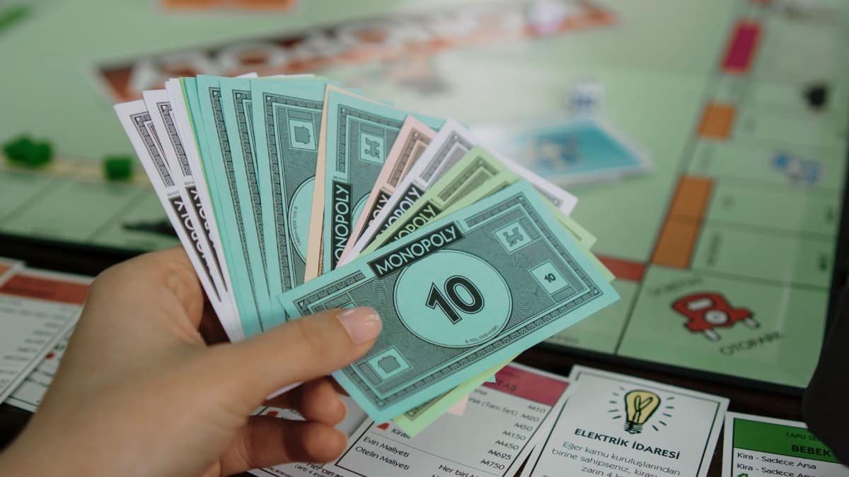 Hand holding colorful Monopoly money over a game board, symbolizing strategy and play.