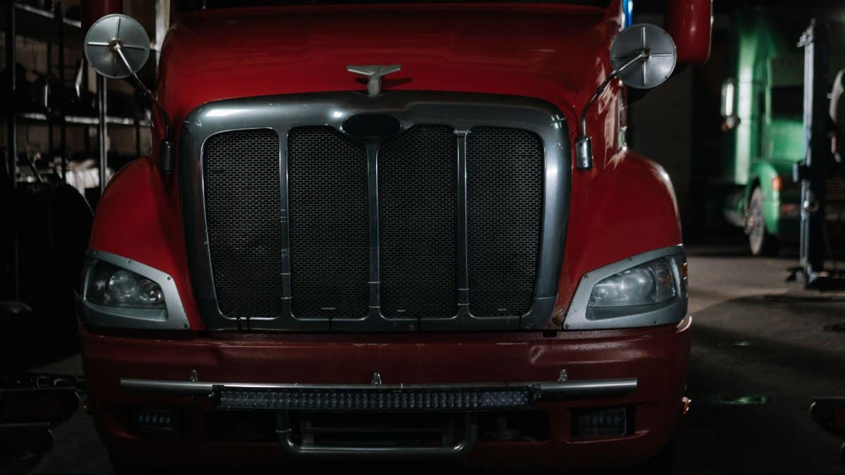 Close-up of a classic red semi truck in a dimly lit garage with chrome details.