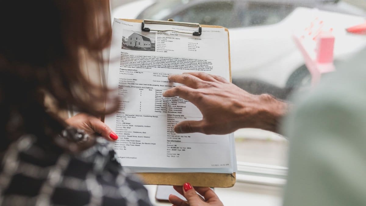Real estate agent discussing property details with client using a clipboard indoors.