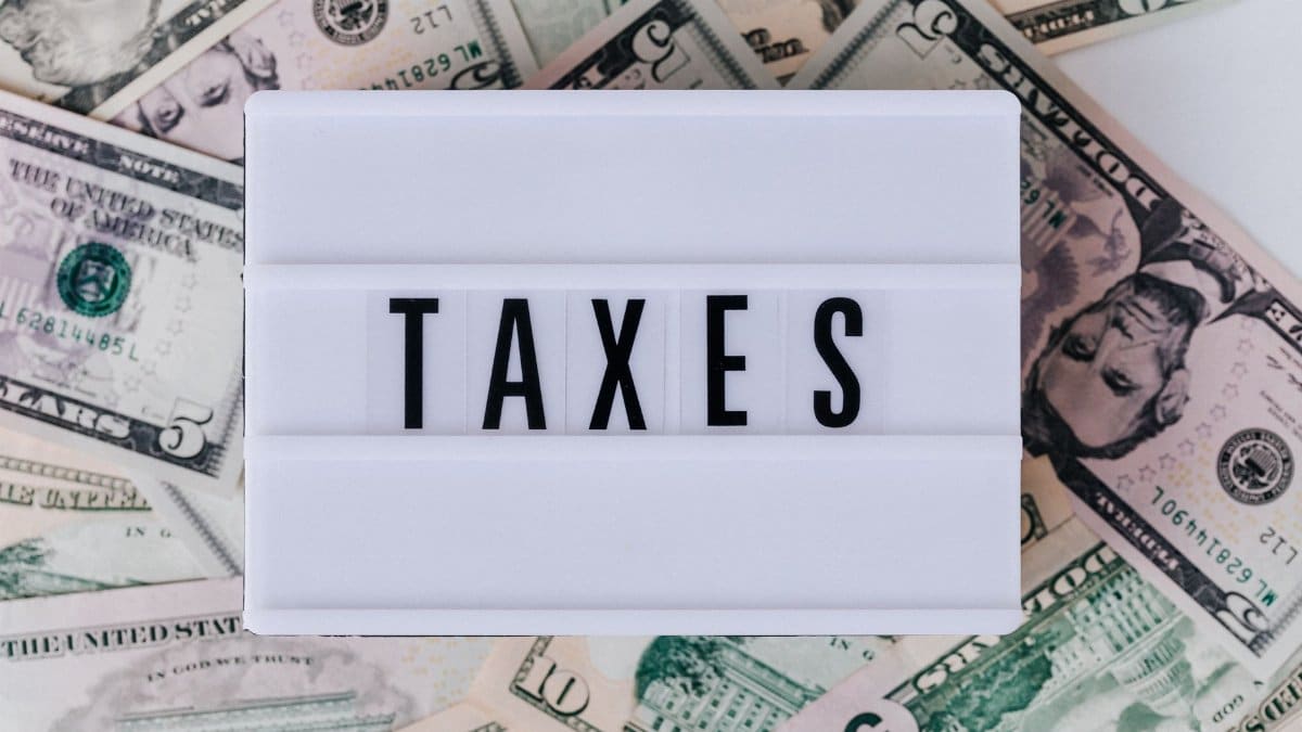 Top view of white vintage light box with TAXES inscription placed on stack of USA dollar bills on white surface