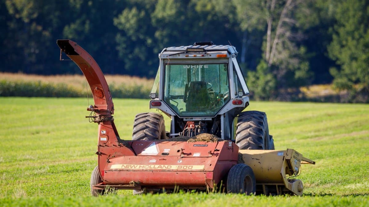 A New Holland 900 tractor operates on a lush green field during a sunny day.