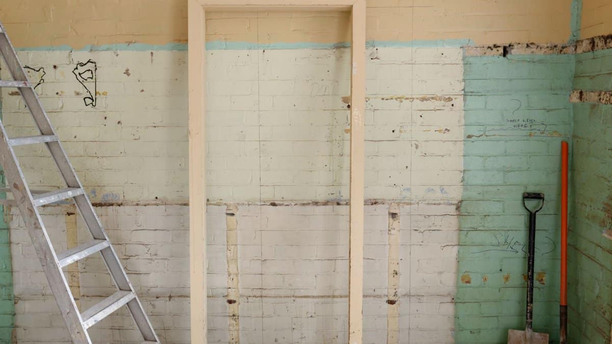 Renovation scene featuring ladder, frame, and tools against partially demolished walls.