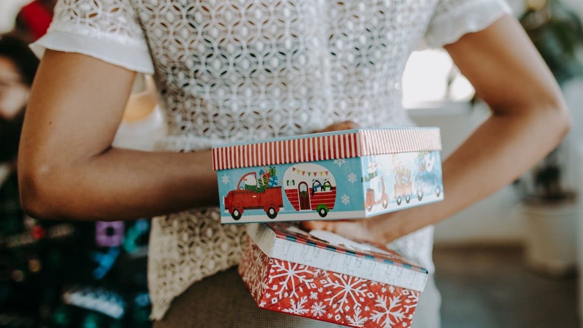 Person hiding colorful Christmas gift boxes behind their back, creating a playful festive surprise.