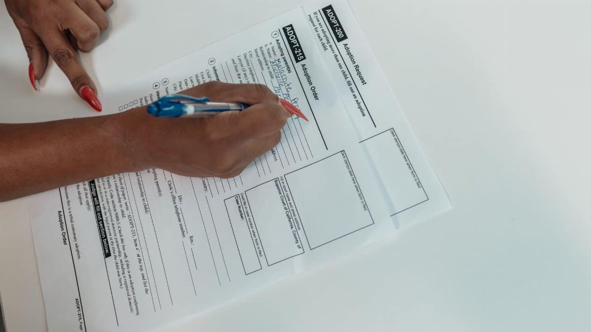 Close-up of a hand filling out an adoption request form with a pen.