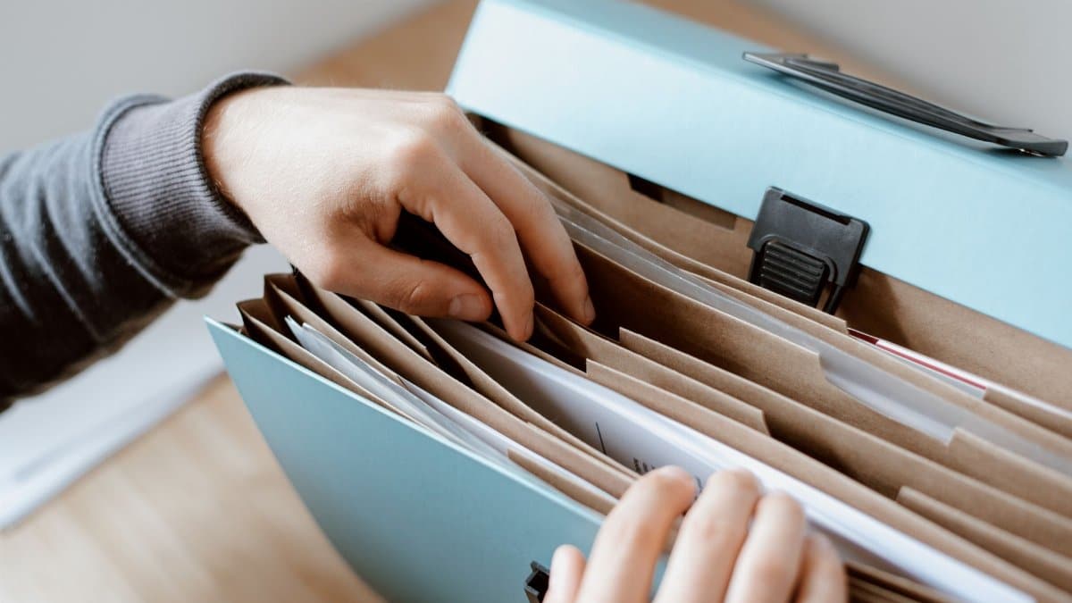 Crop unrecognizable person selecting document in opened briefcase for documents placed on wooden table