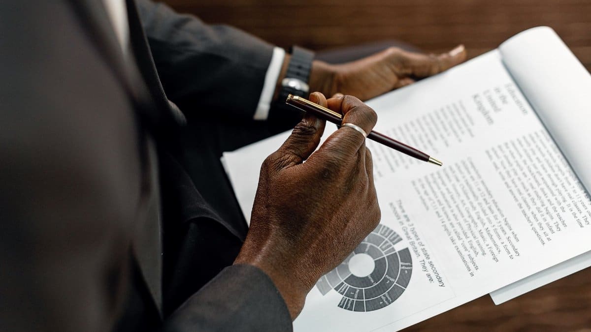 A businessman in a suit reviewing printed documents with a pen, focusing on details.