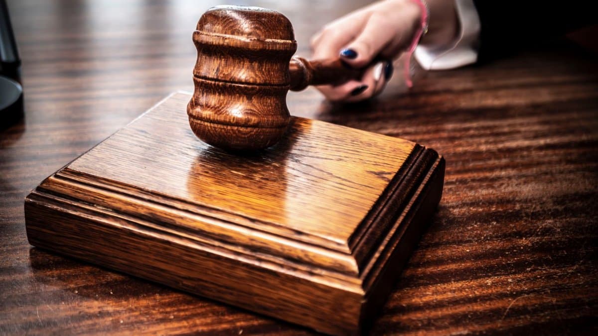 Close-up image of a wooden gavel held by hand on a desk in a courtroom setting.