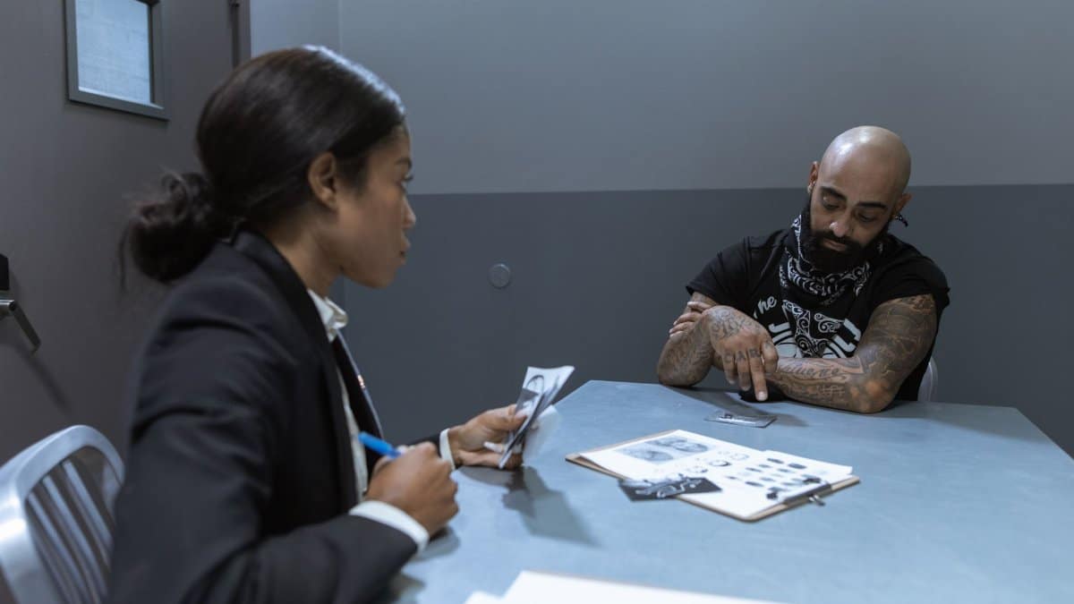 Police officer interrogating a suspect in an investigation room with documents and evidence on the table.