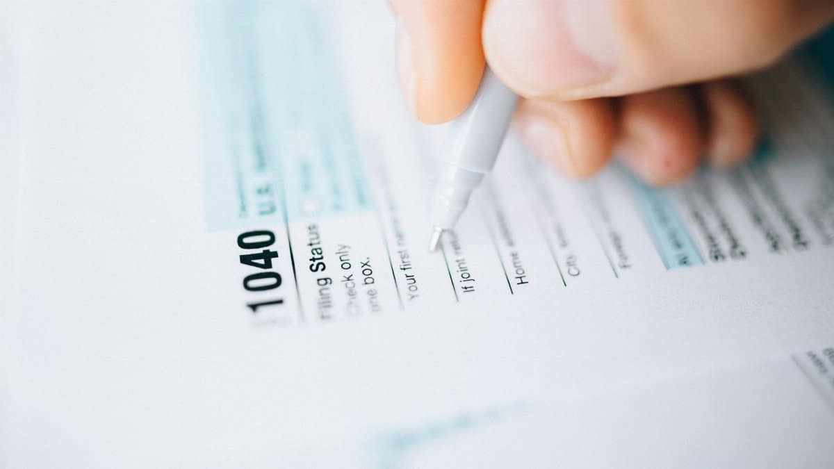 Close-up of a hand using a pen to fill out a tax form 1040, focusing on details.