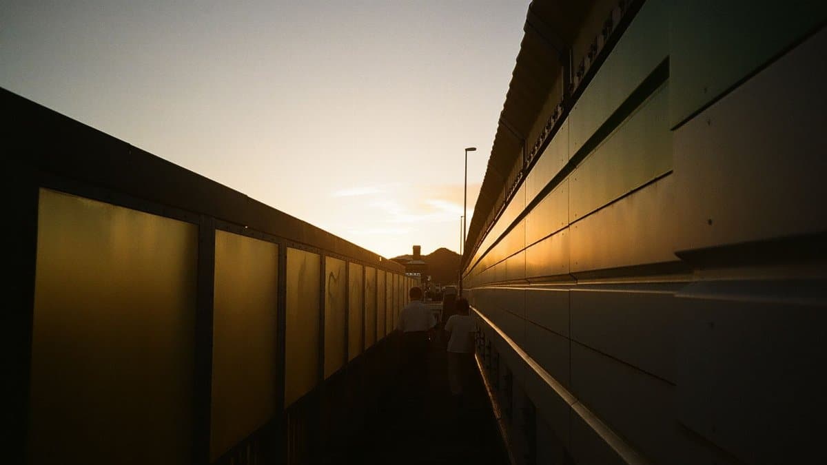 Dramatic sunset casting long shadows in a city alleyway as people walk between reflective walls.
