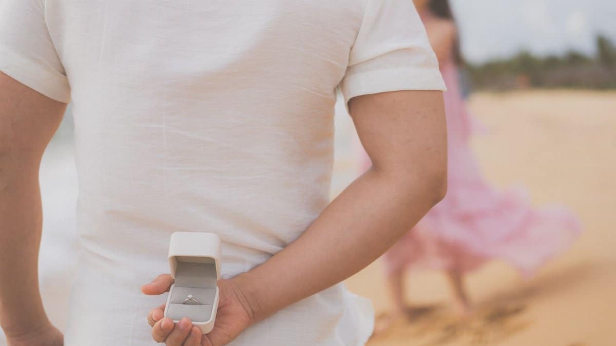 A man hides an engagement ring behind his back, preparing to propose on a beach in Phu Quoc.