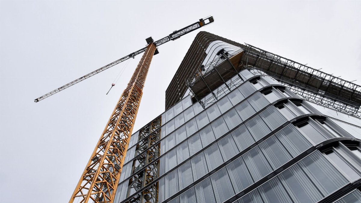 A low angle shot of modern building under construction with a crane viewed against the sky.